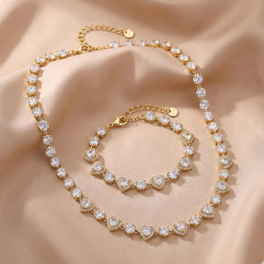 Podroben pogled na lesketajočo zlato zapestnico iz vrste srčastih členov s kamni, kot jo nosi model. Zapestnica je oblikovana tako, da tvori popoln set z biserno ogrlico z zlato pentljo in srčkom.